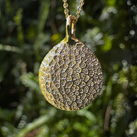 Close up of gold dog's nose print pendant on green leafy background