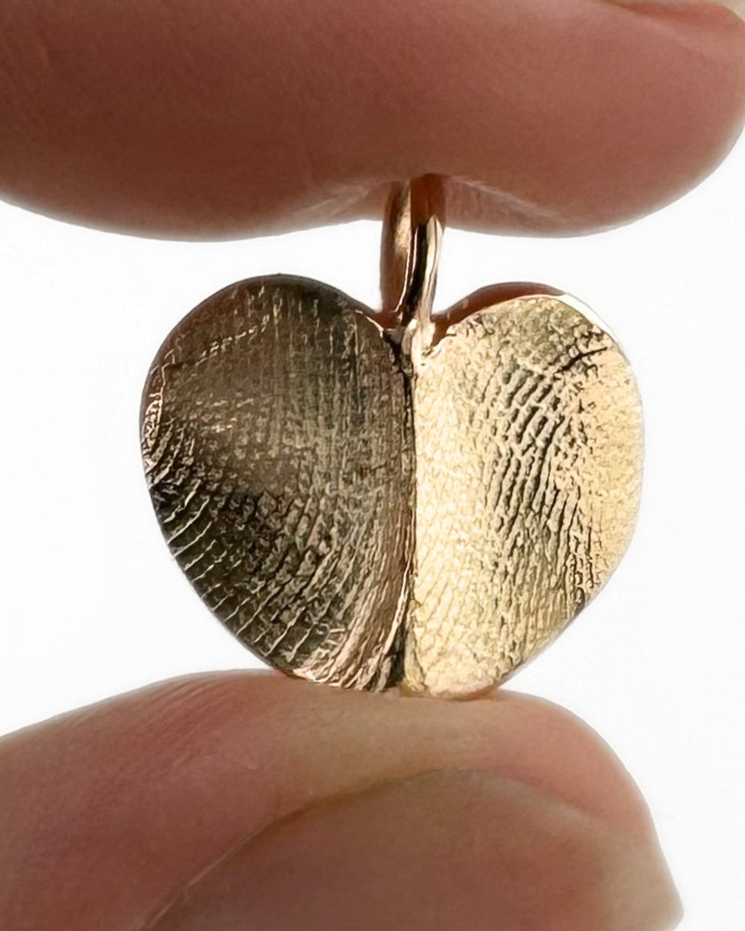 Close up of gold heart pendant with two fingerprint impressions on light grey background