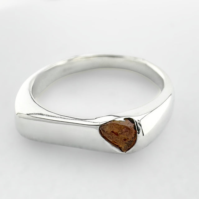 Thin silver signet ring with a honey coloured sapphire on a light grey background
