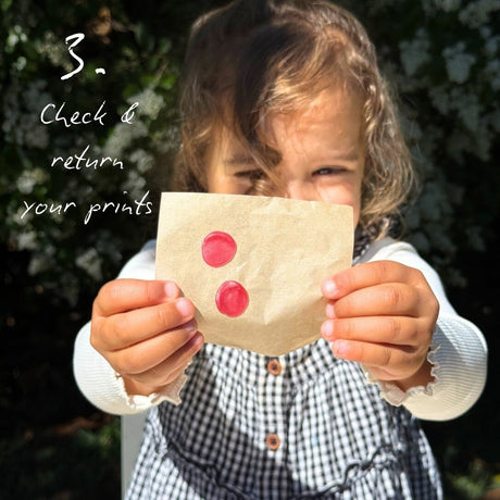 Child outside in a garden holding up a square of paper with two red wax fingerprint impressions