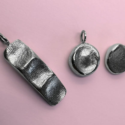 Six silver fingerprint pendants on pink background