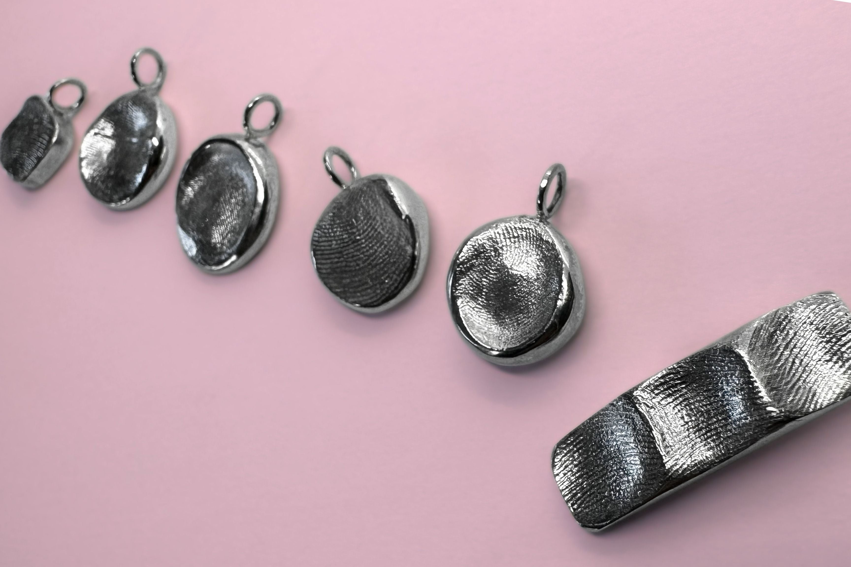 Sterling silver fingerprint pendants on pink background