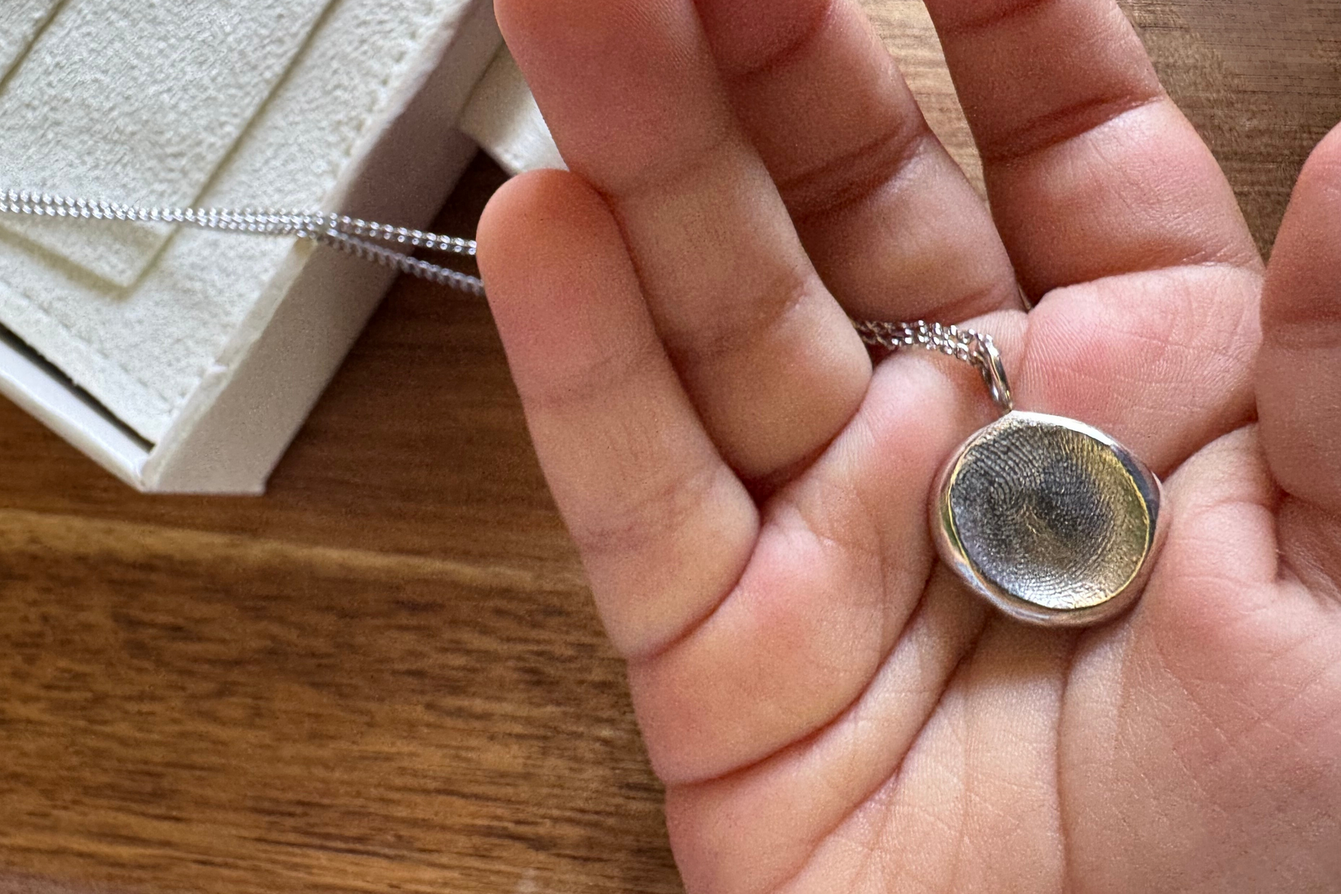 Child holding a silver fingerprint impression pendant