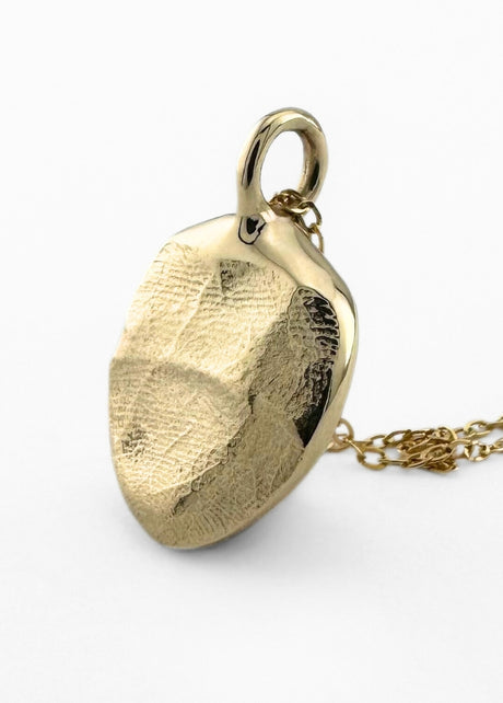 Close up of gold infant fingerprint pendant on light grey background