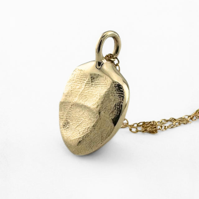 Close up of gold infant fingerprint pendant on light grey background