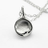Close up of silver fingerprint pendant on light grey background