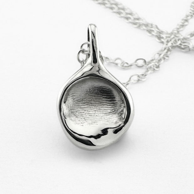 Close up of silver fingerprint pendant on light grey background