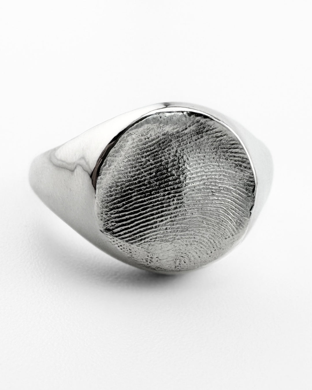 Close-up of large silver signet ring with fingerprint impression on light grey background