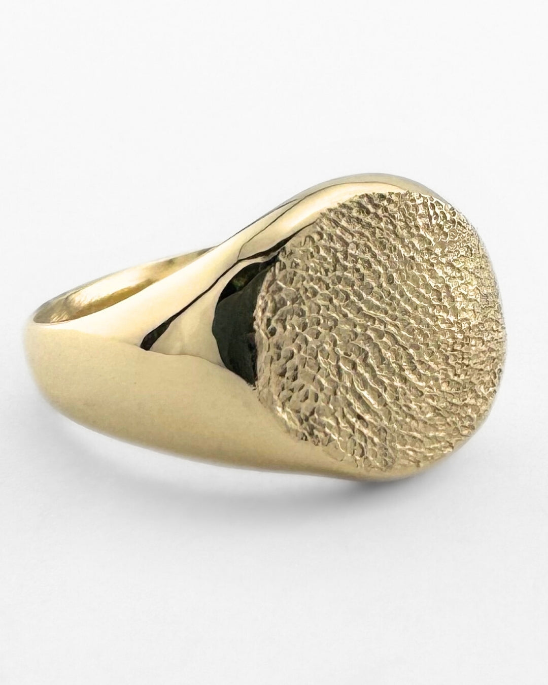 Large gold signet ring with dog's paw print impression on light grey background