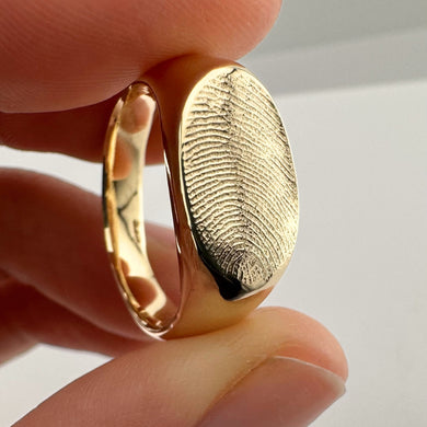 Close up of someone holding a gold fingerprint signet ring