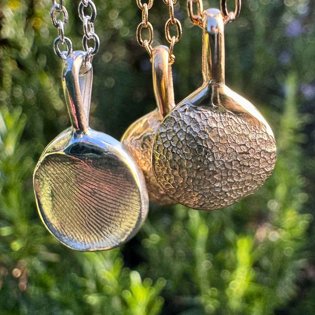 Gold and silver impression print necklaces on a green leafy background
