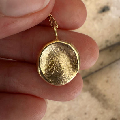 Person holding a gold fingerprint necklace