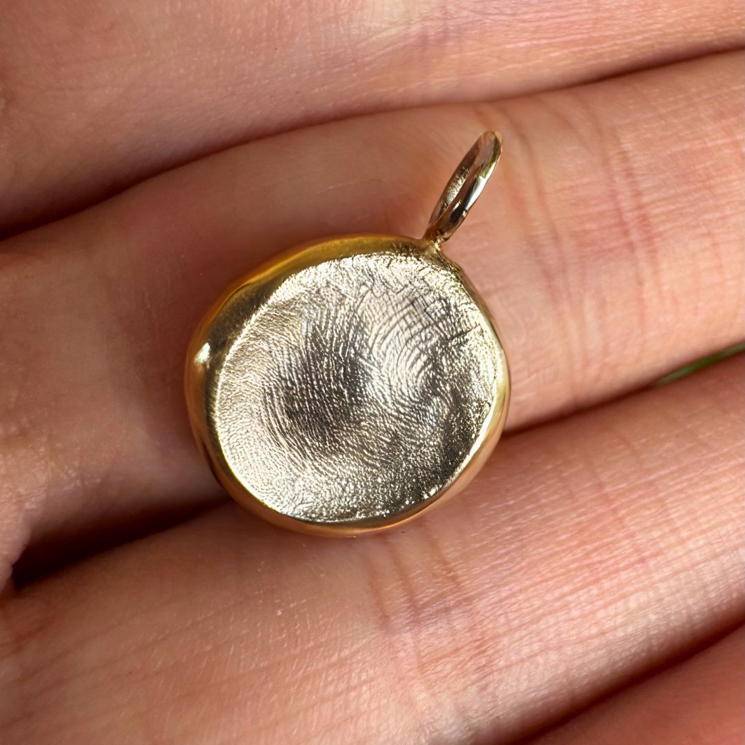 Gold fingerprint pendant on palm of hand