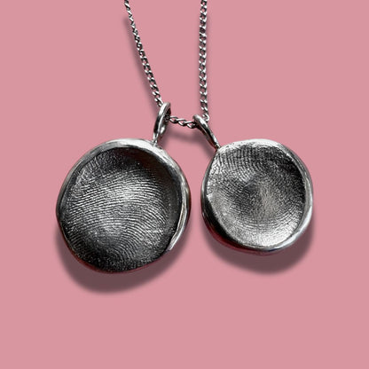 Two sterling silver fingerprint pendants on pink background