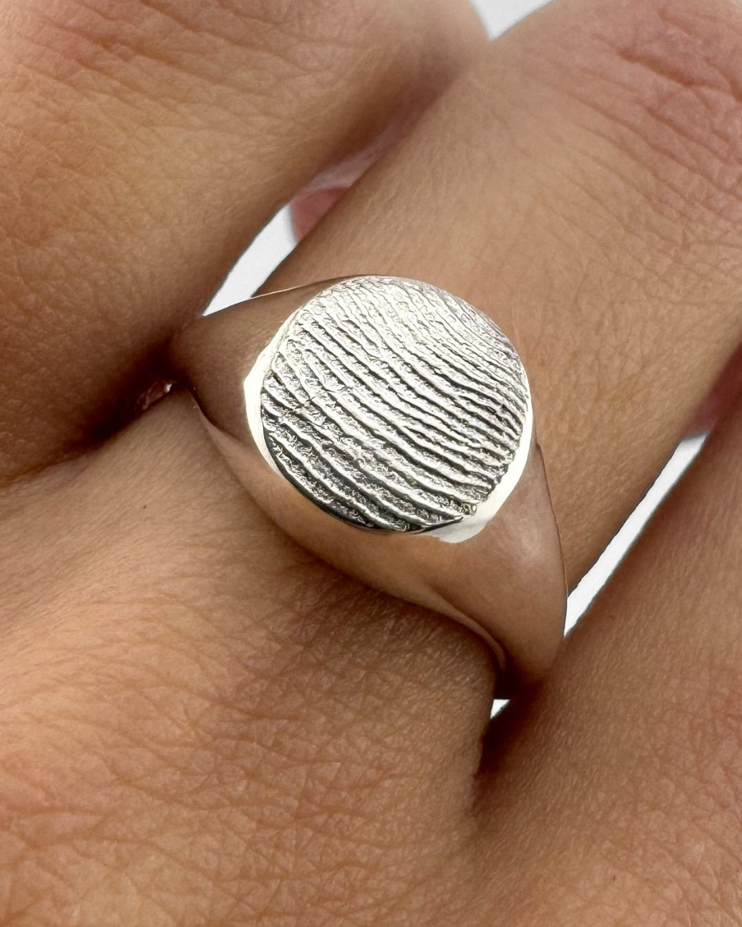 Close up of a hand wearing a small silver signet ring with fingerprint impression