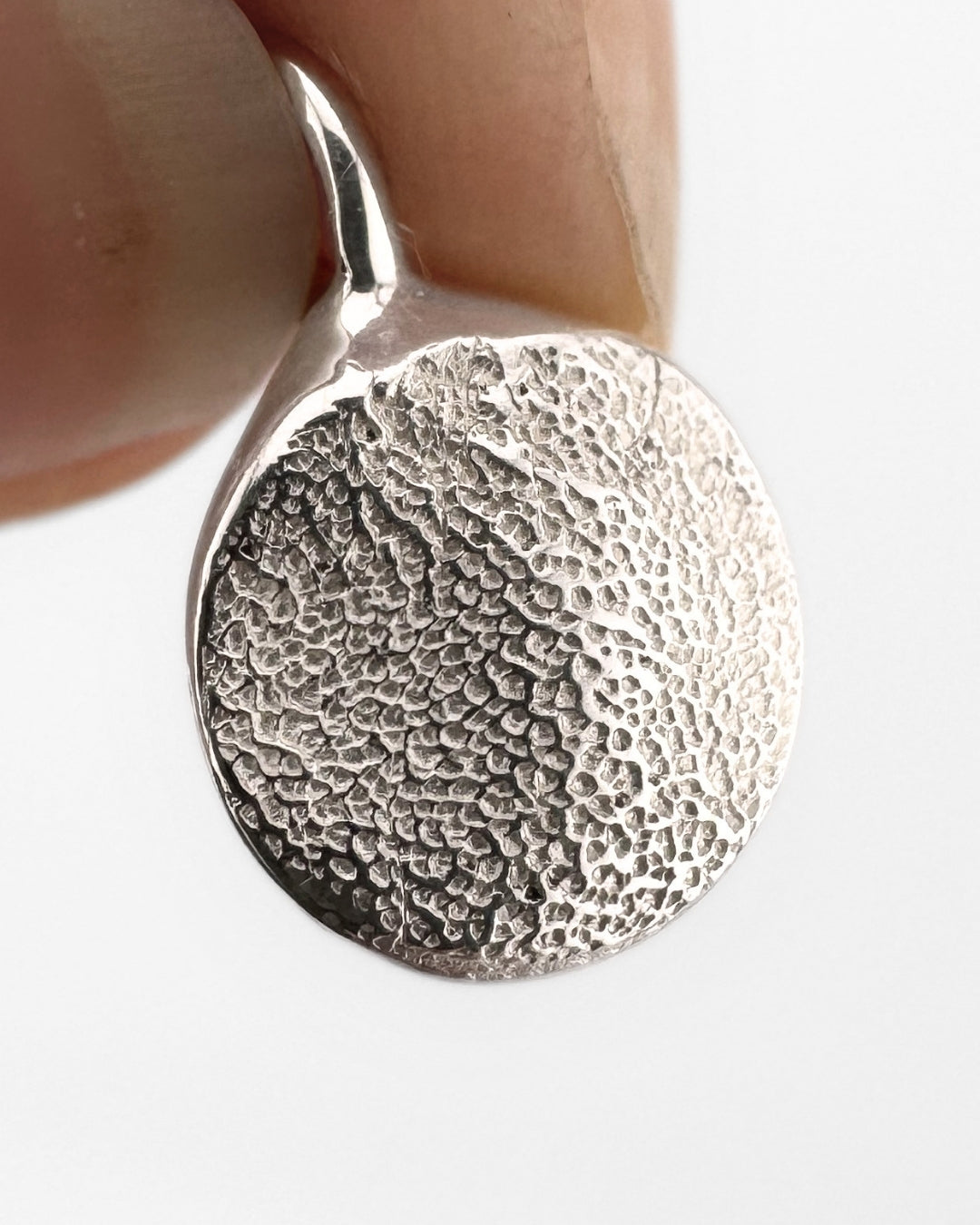 Circular silver pendant with dog's paw print impression on light grey background