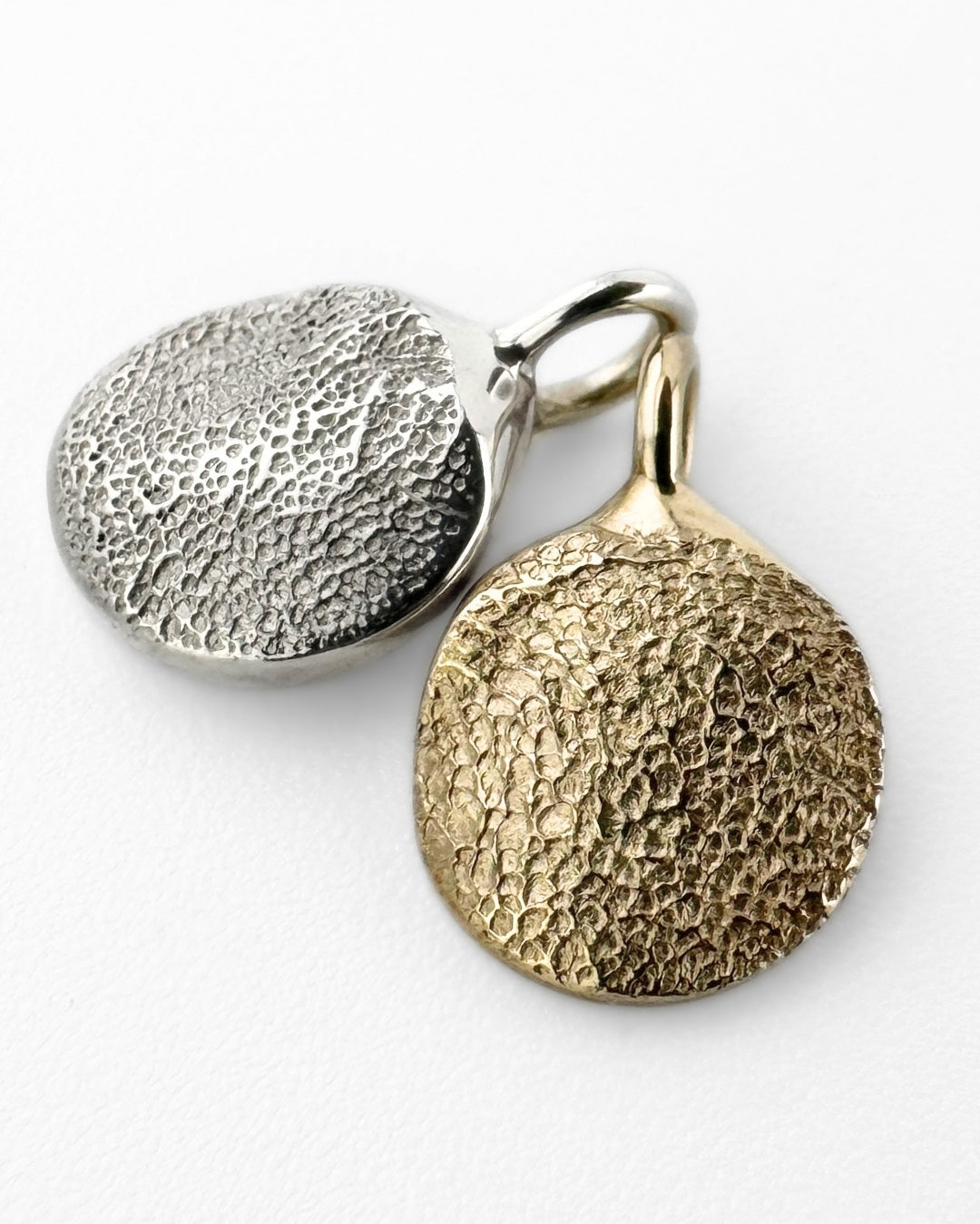 Two paw print impression pendants in gold and silver a on light grey background