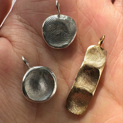 Two silver fingerprint pendants and one gold family fingerprint bar on palm of hand