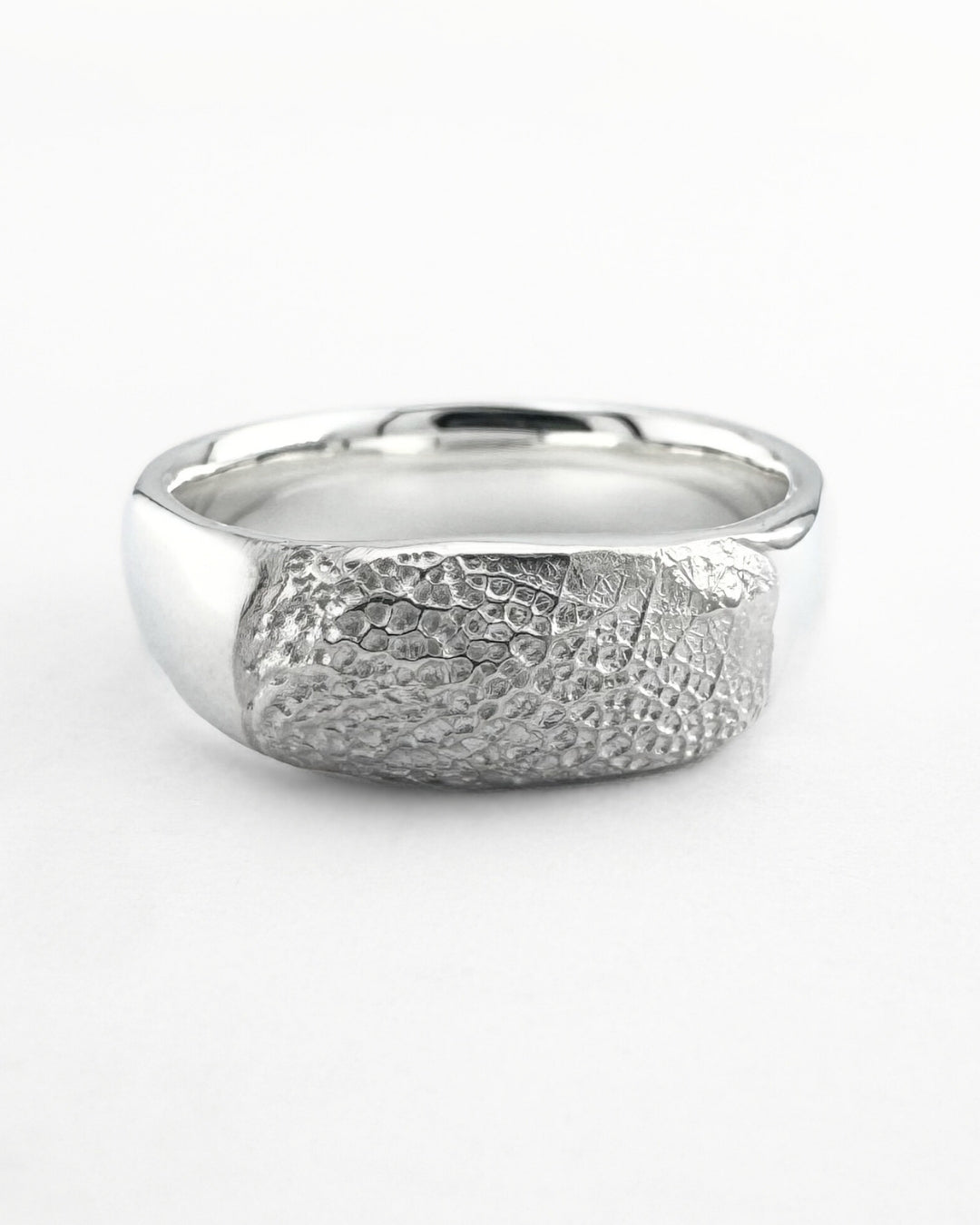 Close-up of silver ring band with a dog's nose print impression on light grey background
