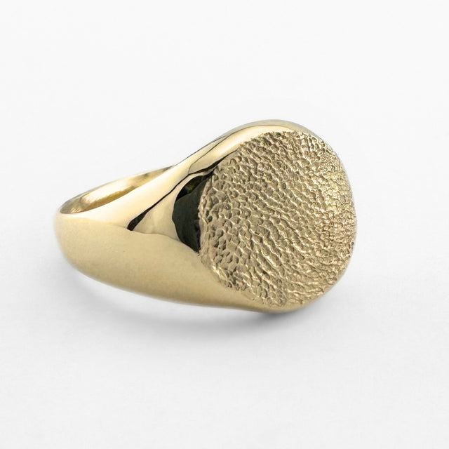 Gold paw print impression signet ring on light grey background