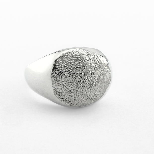 Silver paw print impression signet ring on light grey background