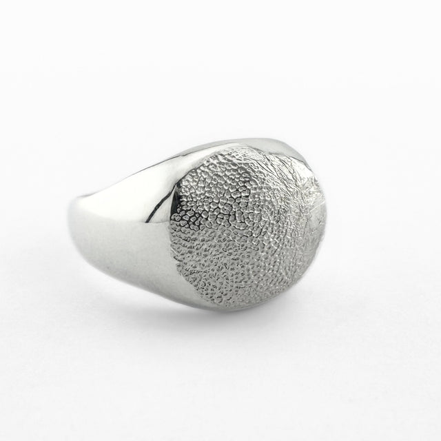 Silver paw print impression signet ring on light grey background