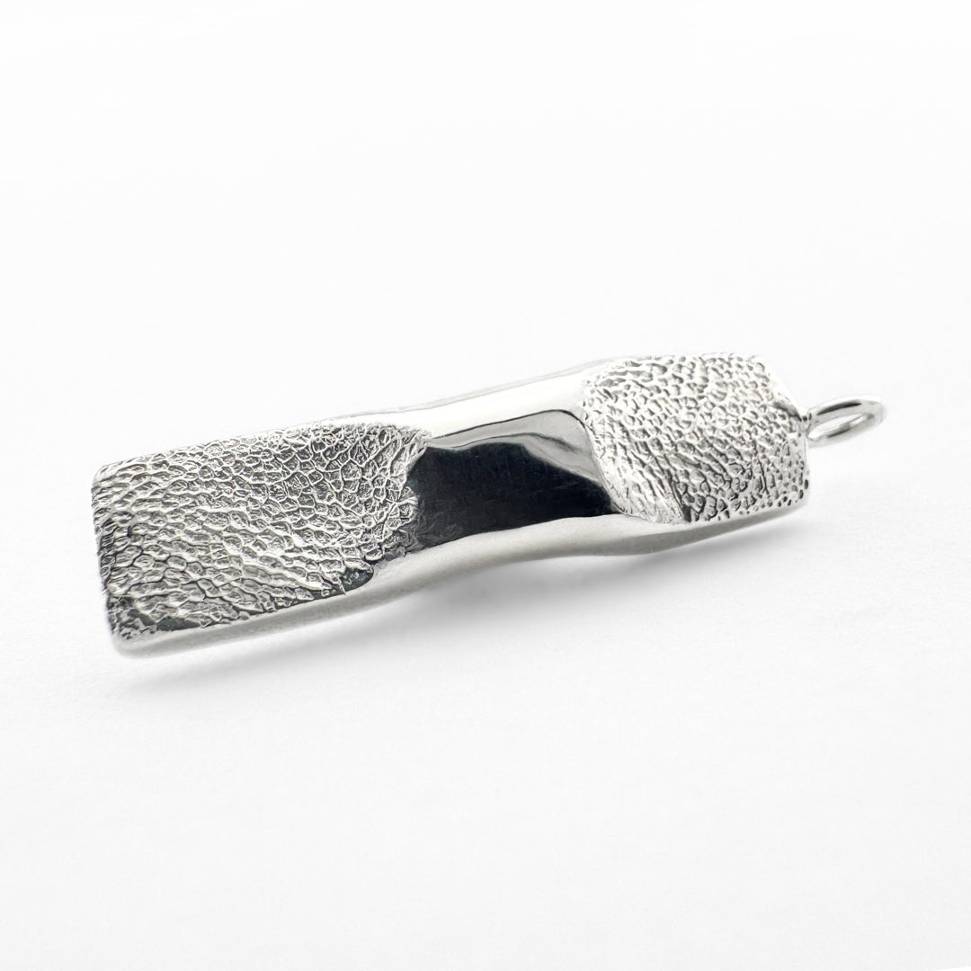Close up of silver dog paw print  pendant on light grey background