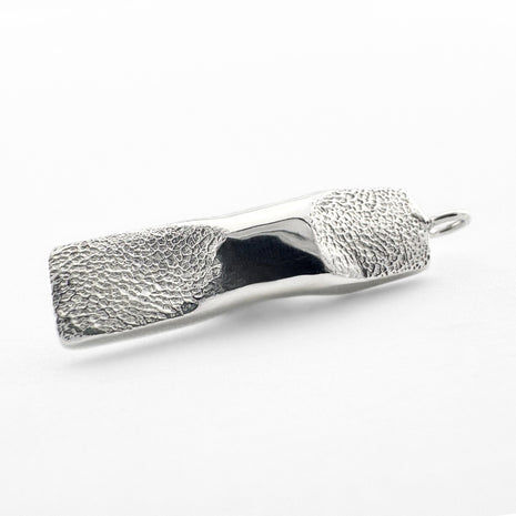 Close up of silver dog paw print  pendant on light grey background