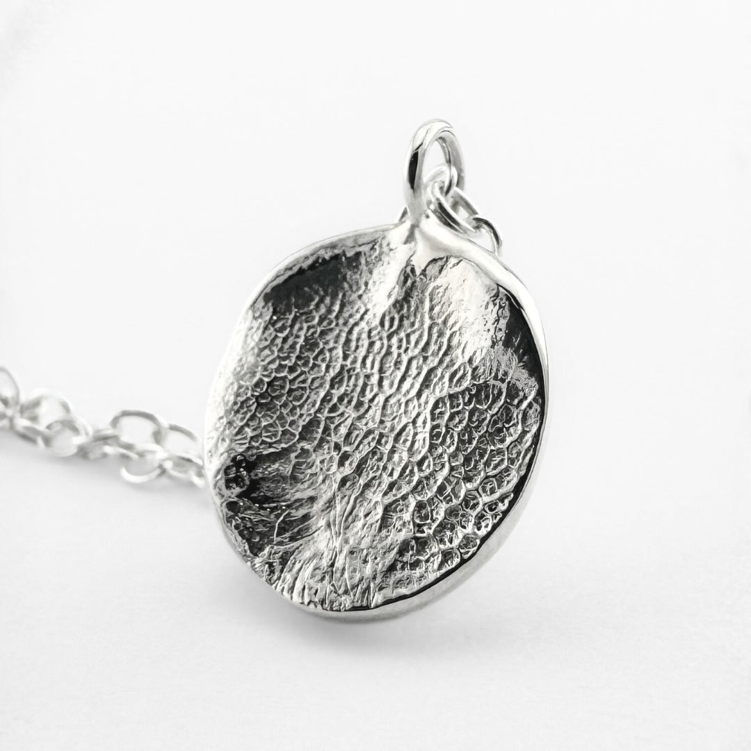 Close up of silver dogs nose print pendant on light grey background