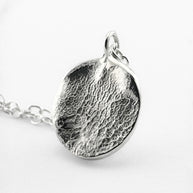 Close up of silver dogs nose print pendant on light grey background