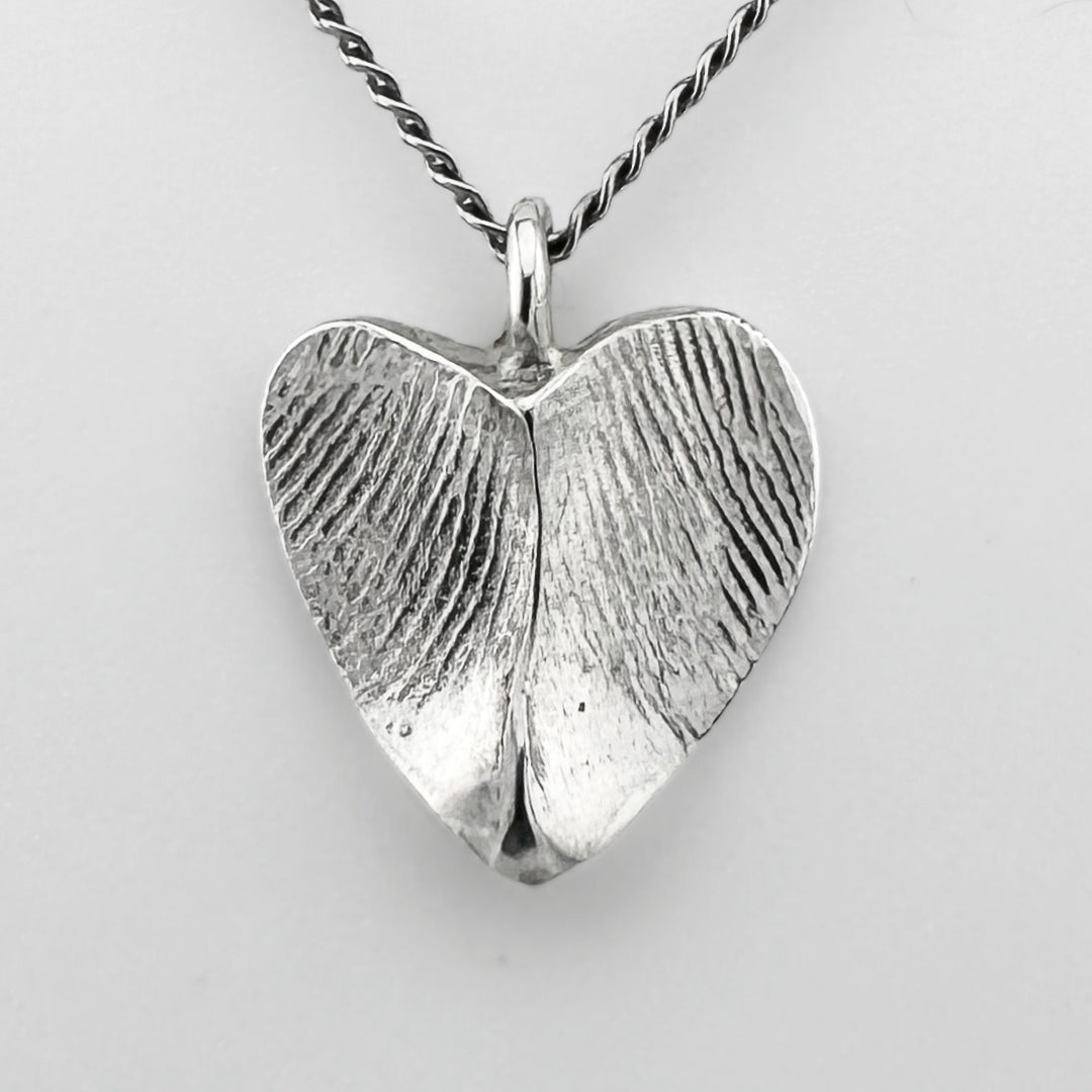 Silver heart-shaped pendant with fingerprint impressions against a light grey background