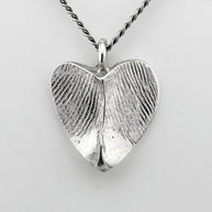 Silver heart-shaped pendant with fingerprint impressions against a light grey background
