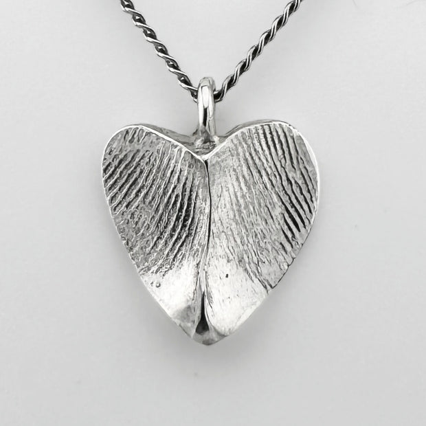 Silver heart-shaped pendant with fingerprint impressions against a light grey background