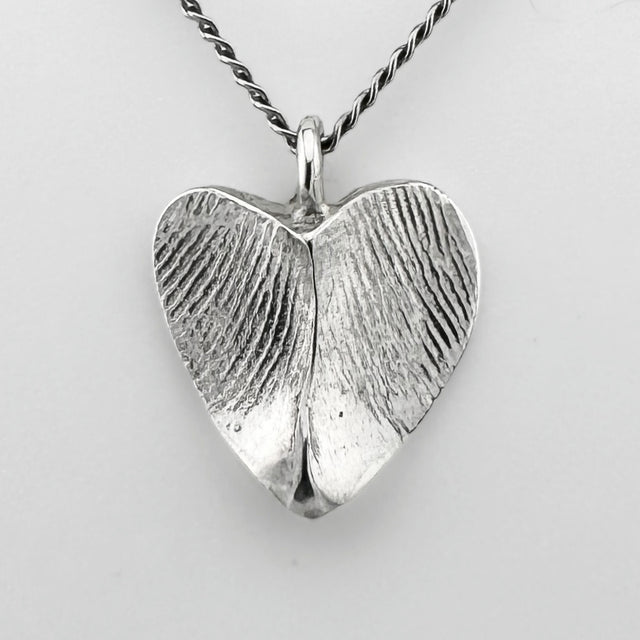Silver heart-shaped pendant with fingerprint impressions against a light grey background