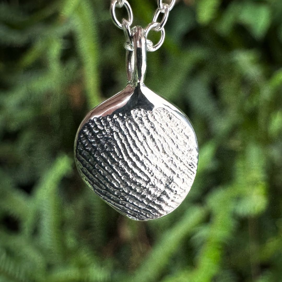 Close up of silver fingerprint pendant on green leafy background
