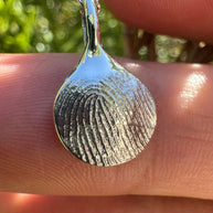 Close up of silver fingerprint pendant on green leafy background