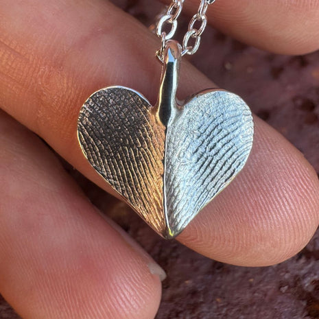 Close up of heart shaped silver fingerprint pendant on deep rust coloured background