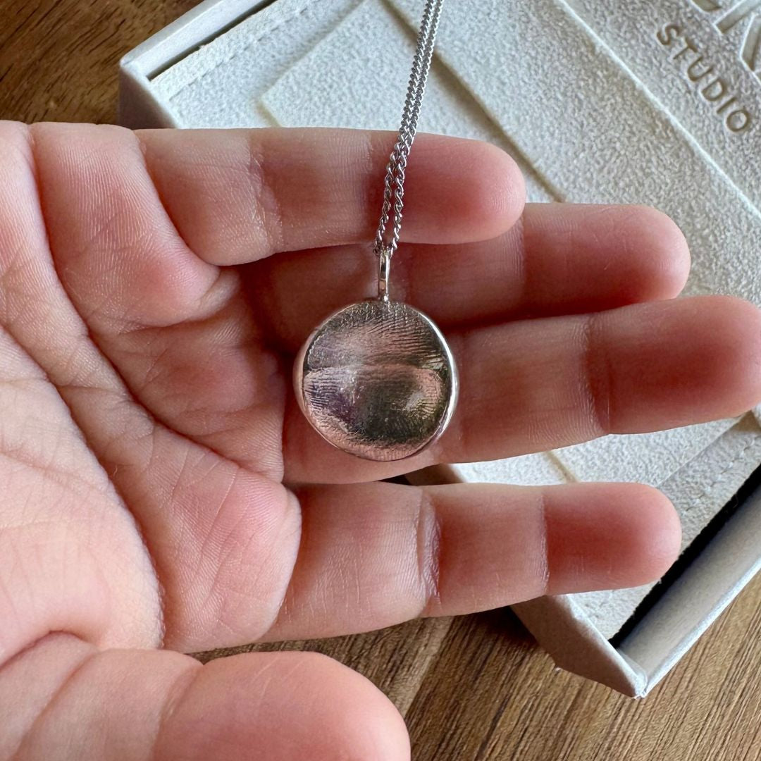 Close up of child holding a silver infant fingerprint pendant