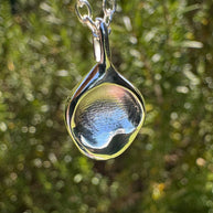 Close up of silver infant fingerprint pendant on green leafy background