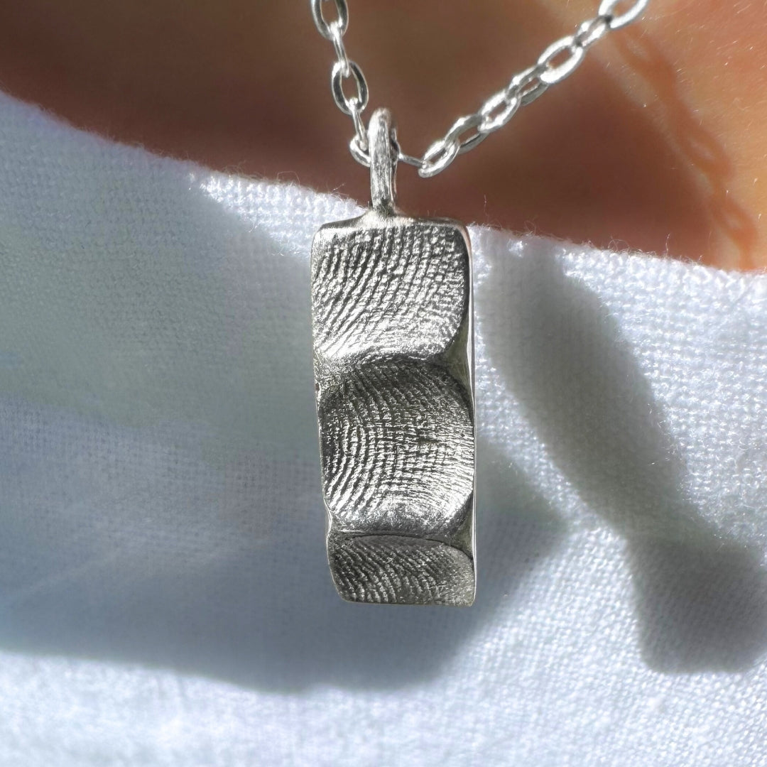 Close up of person wearing a silver family fingerprint necklace