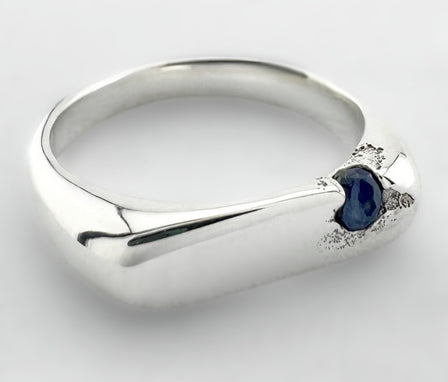 Thin silver signet ring with a blue sapphire on a light grey background