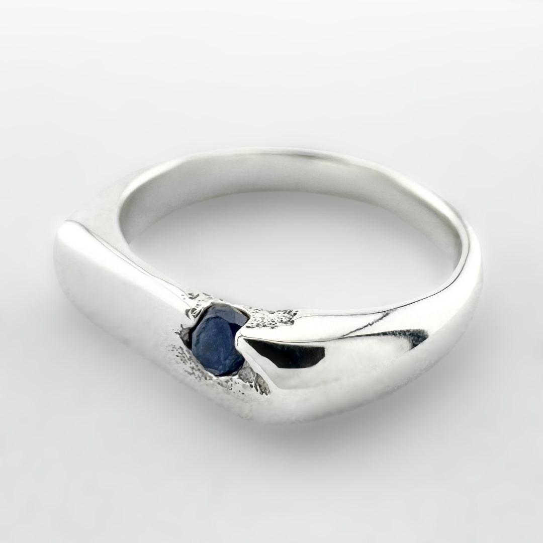 Thin silver signet ring with a blue sapphire on a light grey background