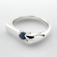 Thin silver signet ring with a blue sapphire on a light grey background