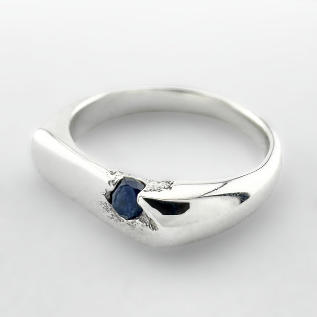 Thin silver signet ring with a blue sapphire on a light grey background