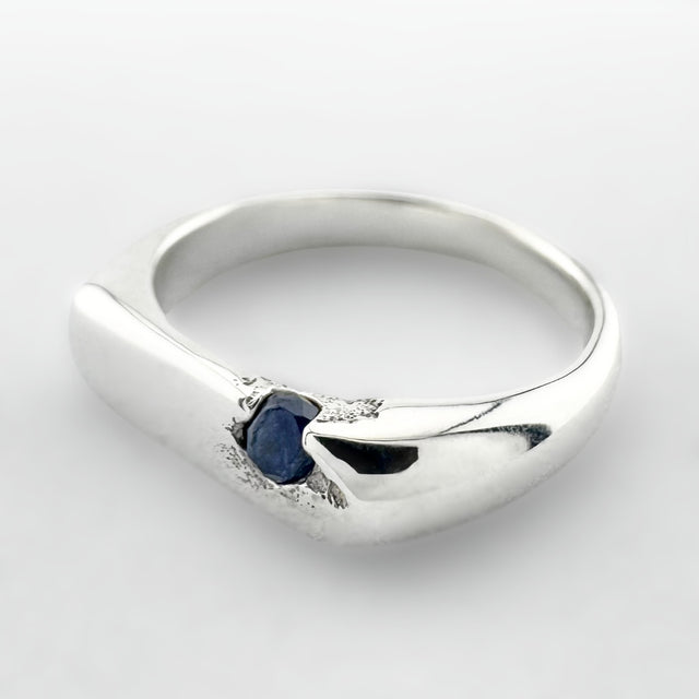 Thin silver signet ring with a blue sapphire on a light grey background