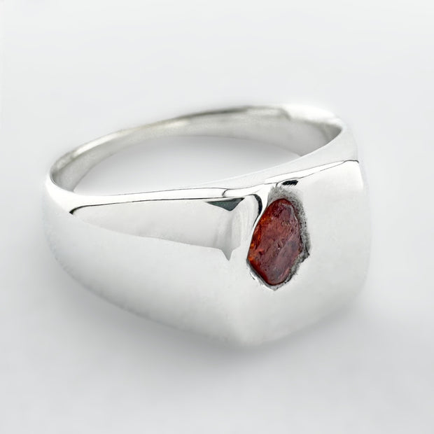 Silver signet ring with an orange sapphire on a white background
