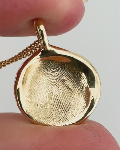 Close up of gold fingerprint pendant on light grey background