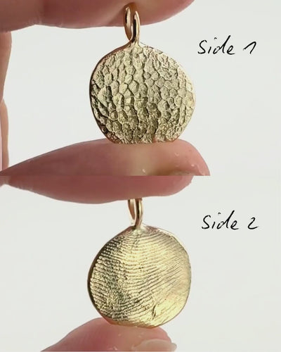 Split screen of the front and back of a gold pendant with a dog's nose print on one side and fingerprint on the other